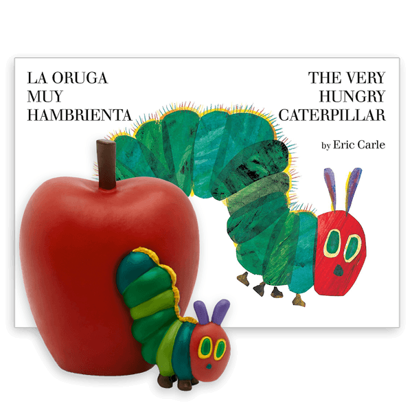 A bilingual edition of Eric Carle&rsquo;s 'The Very Hungry Caterpillar' (La Oruga Muy Hambrienta) accompanied by a caterpillar figurine emerging from a large red apple.