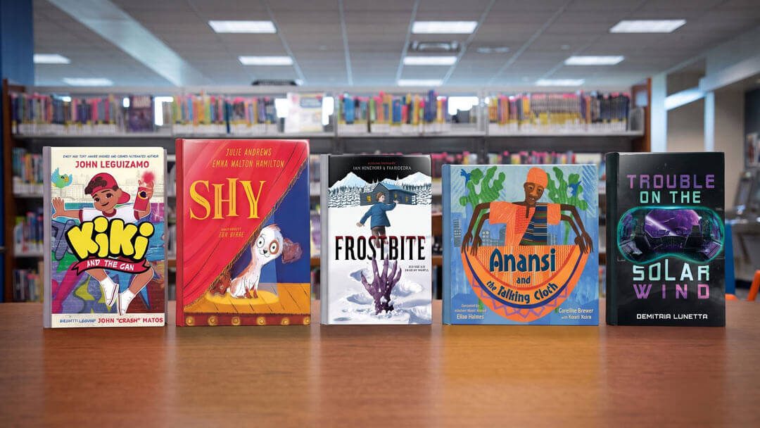 Kiki and the Gan by John Leguizamo, Shy by Julie Andrews, Frostbite, Anansi and the Talking Cloth, Trouble on the Solar Wind by Demitria Lunetta books on library table.